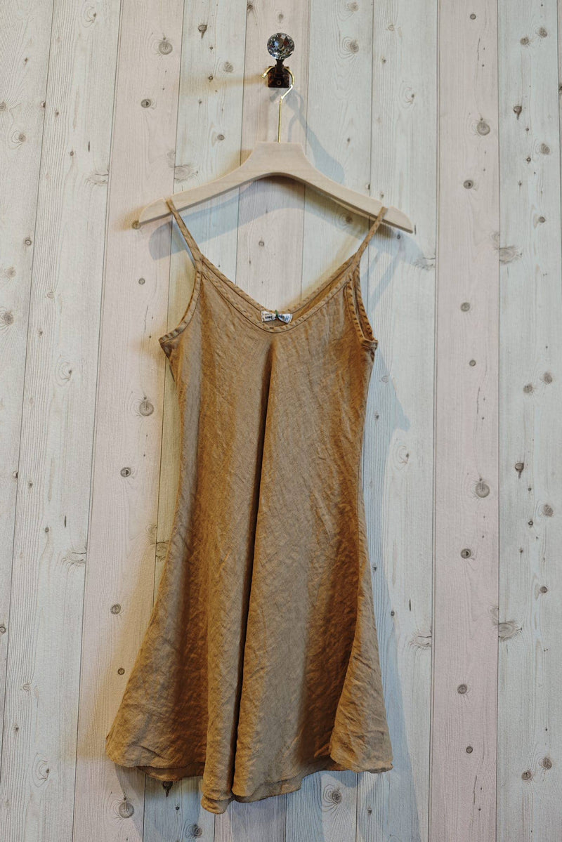 Gold slip dress hanging on a wooden hanger against a wooden wall.