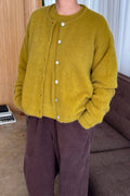 Person wearing a mustard yellow cardigan with white buttons indoors.