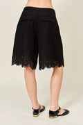 Black lace-trimmed shorts worn by a person on a plain background