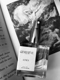 Perfume bottle labeled 'Genevéve Lunéa' on a surface with artistic background
