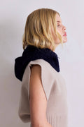 Woman wearing a beige sleeveless sweater with a navy blue scarf around her neck against a plain background