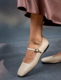 Beige flat shoes with a strap worn by a person on a gray background