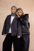 Two people wearing dark coats and hats against a beige background