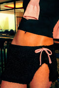 Person wearing black shorts with pink drawstring and pink top in a blurred indoor setting